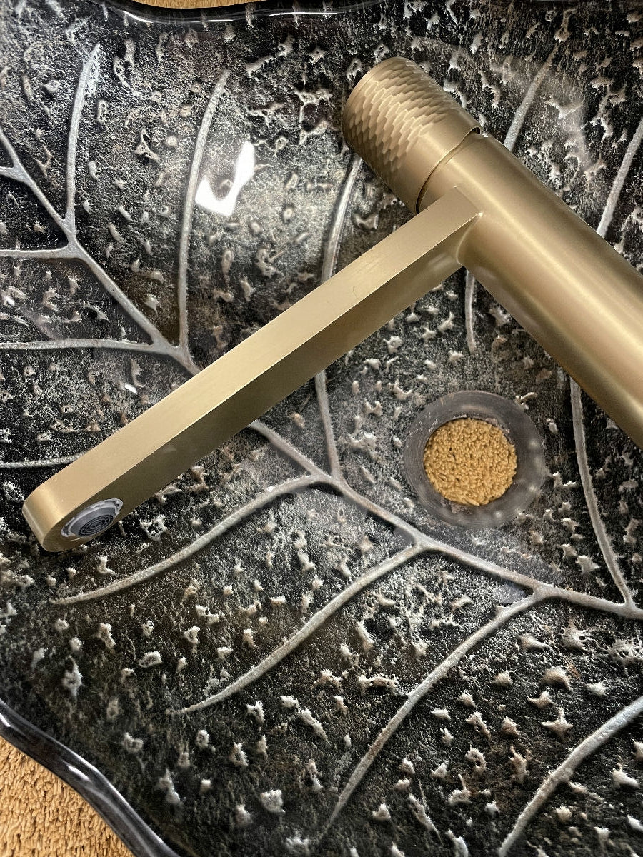 Šedé umyvadlo ve tvaru listu se zlatou baterií